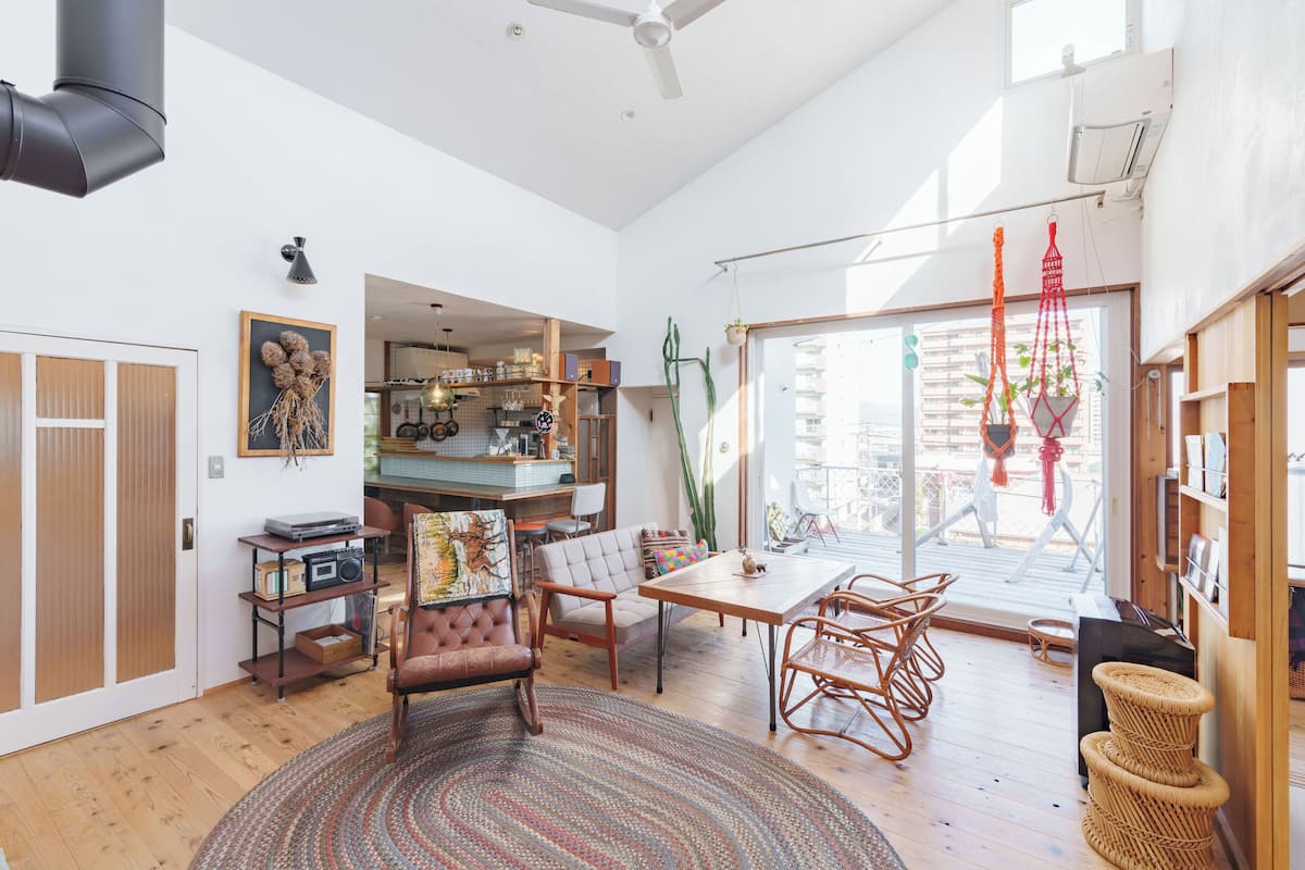 A spacious living room with a large window, a dining area, and a kitchen visible through an open door.