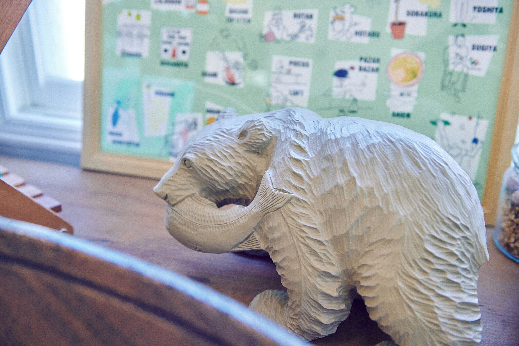 A sculpture of an elephant on a wooden surface with a bulletin board in the background.