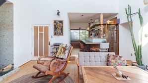 A spacious living area with a wooden dining table, a rocking chair, and a sofa. There is a kitchen area with wooden cabinets and a window overlooking the garden. - SMALL TOWN HOTEL Hakodate (Hakodate)