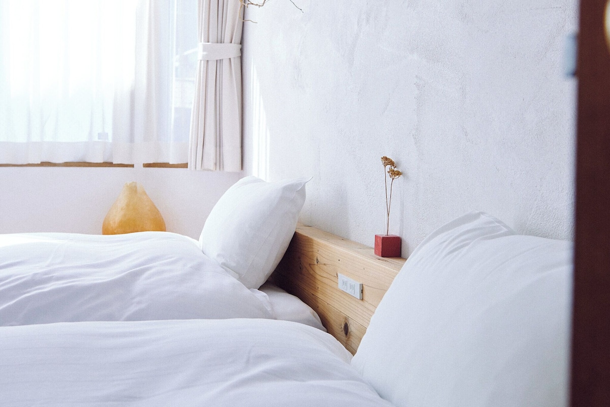 A bedroom with a wooden headboard, white bedding, and a small vase with dried flowers.