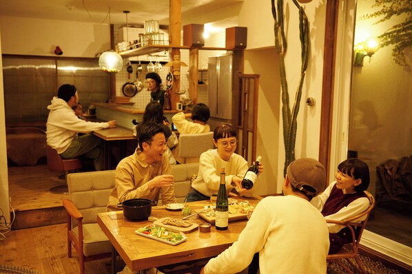 A group of people dining at a wooden table in a cozy, well-lit room with a modern kitchen in the background. - SMALL TOWN HOTEL Hakodate (Hakodate)