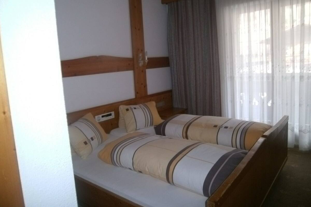 A room with a wooden ceiling, a bed with striped bedding, and a window with curtains.