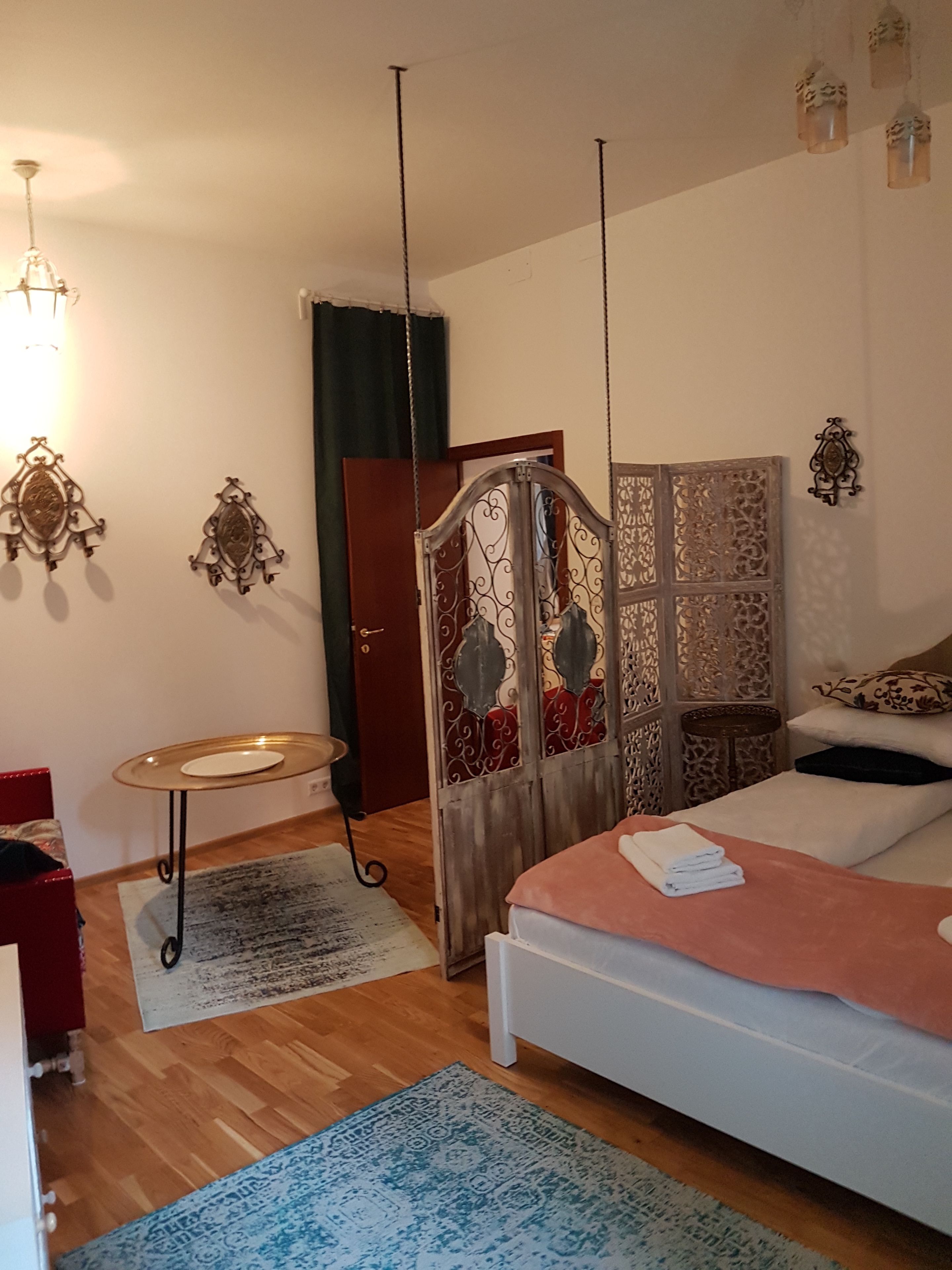 A bedroom with a bed, a small table, a chair, a wardrobe, and a decorative partition.
