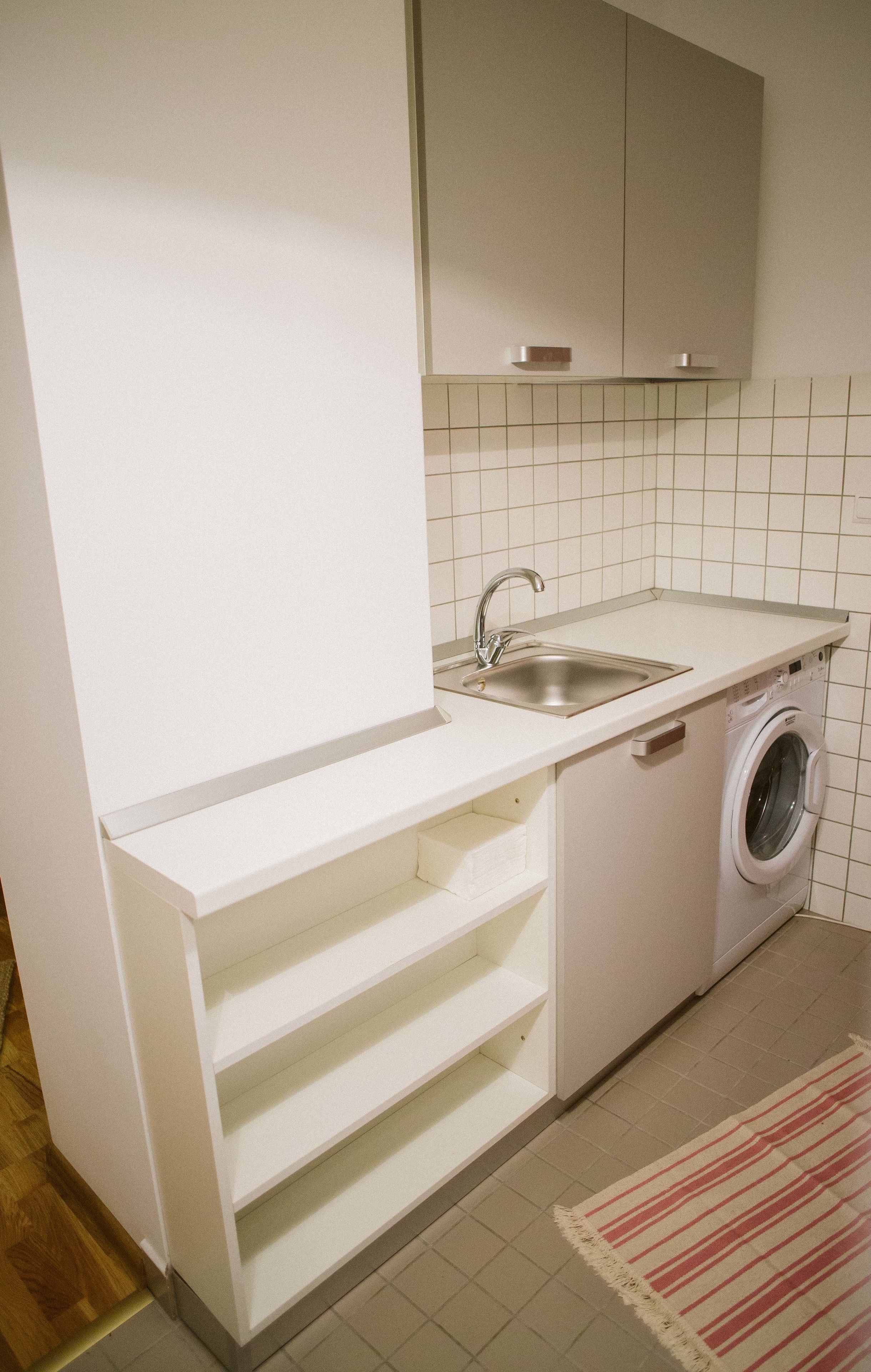 Eine kleine Küche mit Spüle, Waschmaschine und einer eingebauten Schrankwand.