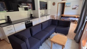 Un espacio habitable moderno con cocina, un sofá seccional azul oscuro, una pequeña mesa de madera y una alfombra gris con textura.