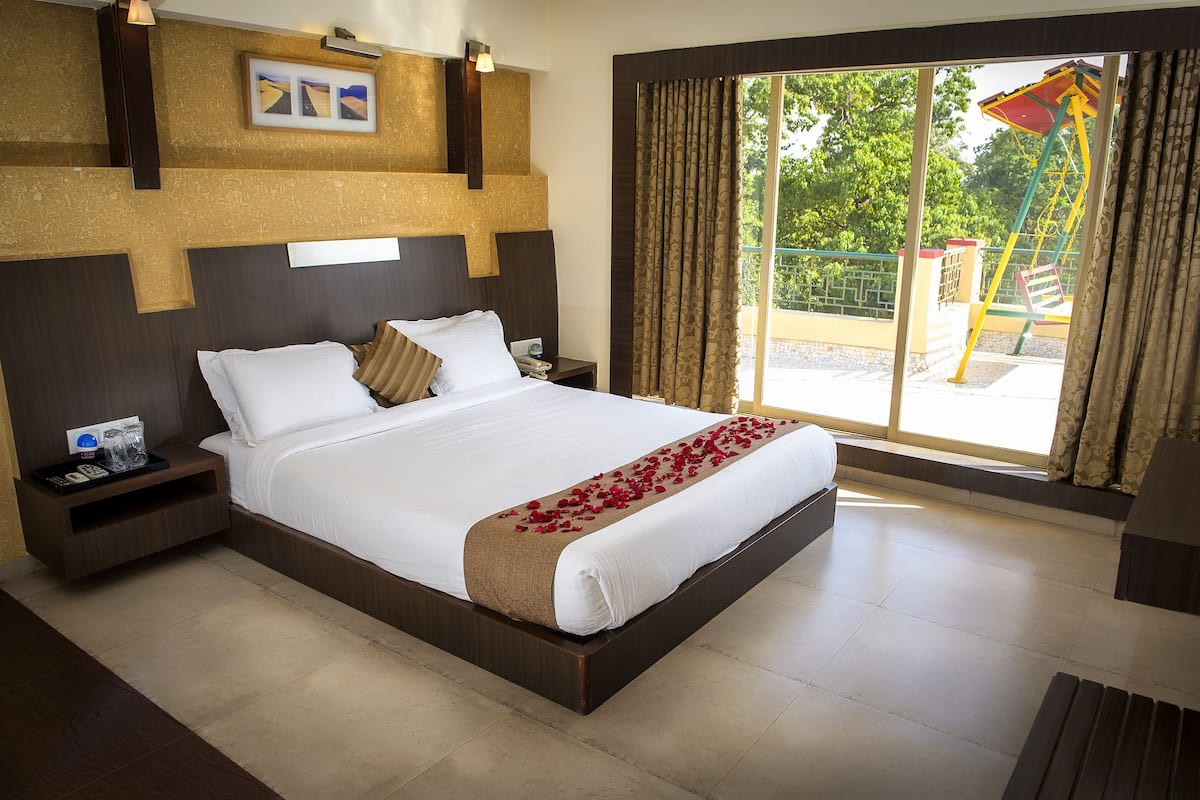 A hotel room with a large bed, a nightstand, a bedside table, a window with curtains, and a view of the outside.