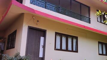 Two-story building with a flat roof and balcony, featuring a garden area and a welcoming entrance.