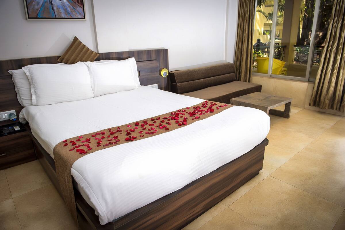 A hotel room with a large bed, a sofa, a small table, and a window with curtains.