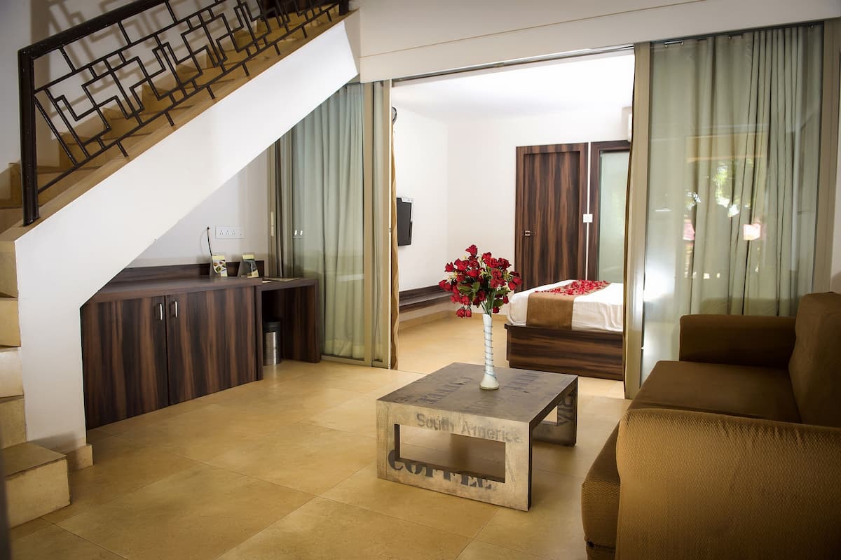 A hotel room with a staircase, a sofa, a coffee table with a vase, and a bed with a window view.