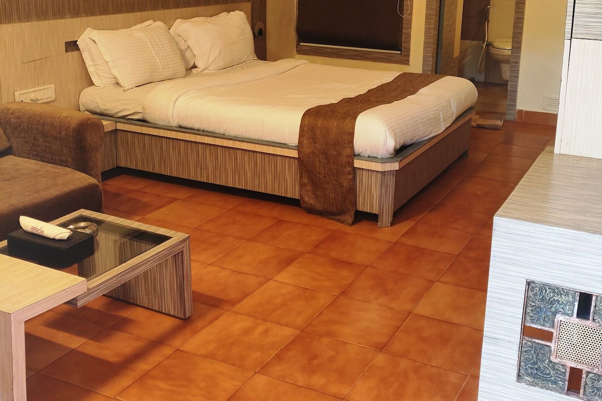 A hotel room with a bed, a sofa, a small table, and a bathroom visible through an open door.