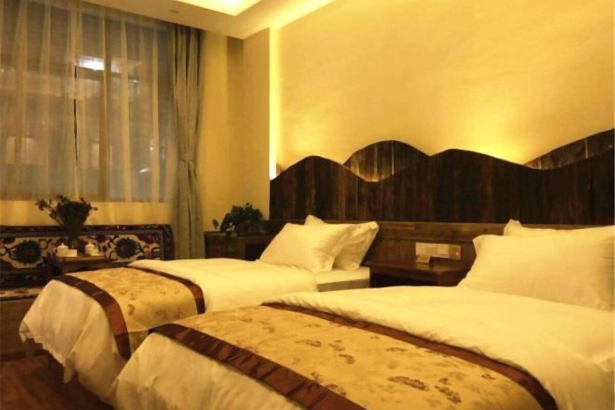 A hotel room with two beds, a large window with curtains, and a wooden headboard.