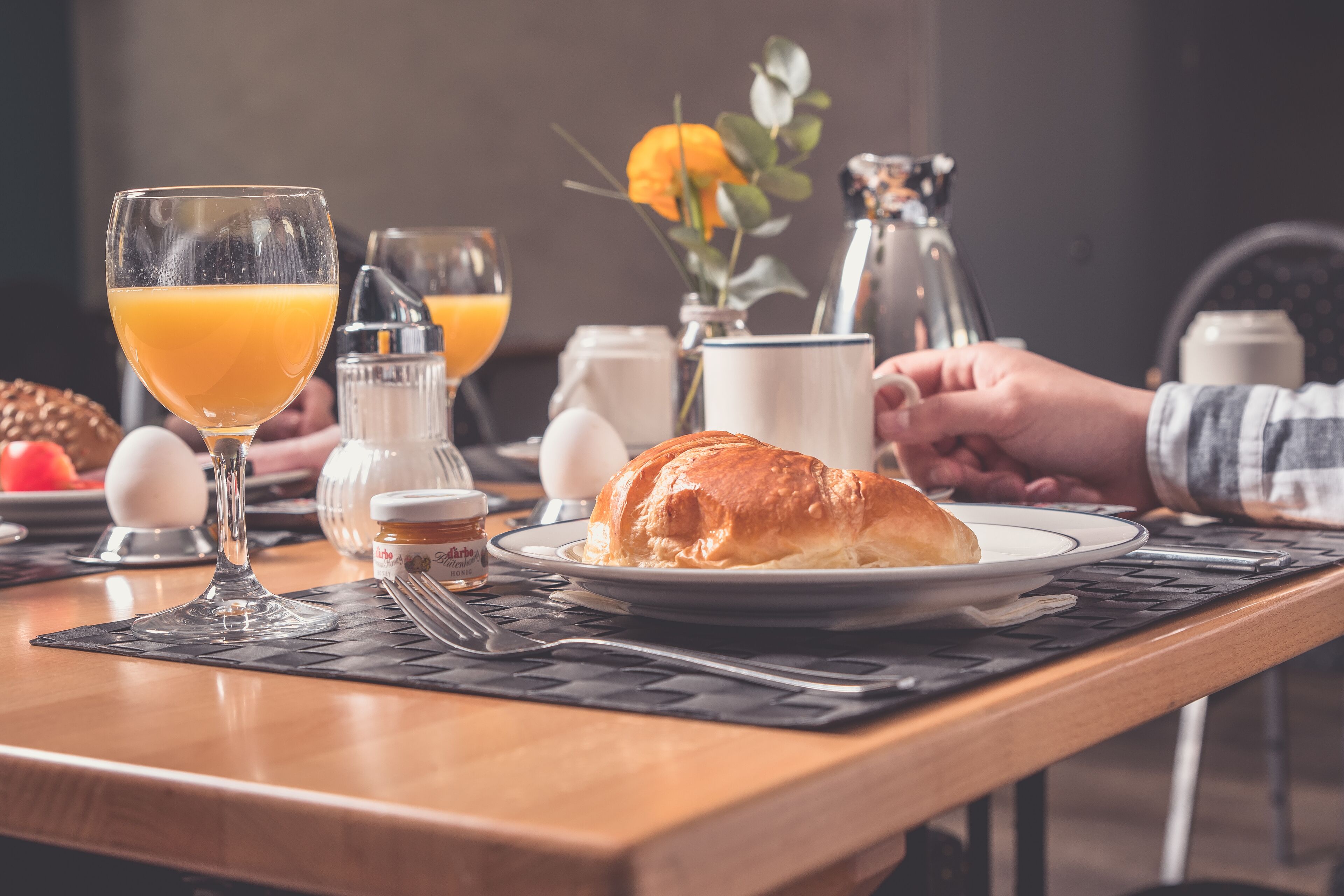 A breakfast setting with a croissant, orange juice, and a coffee pot on a wooden table.