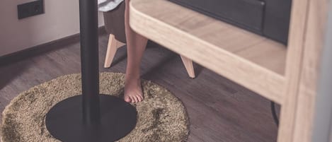 Una persona con bata blanca sentada a una mesa redonda con una computadora portátil, una taza y una planta pequeña. Hay una cafetera sobre un mueble de madera junto a la mesa.