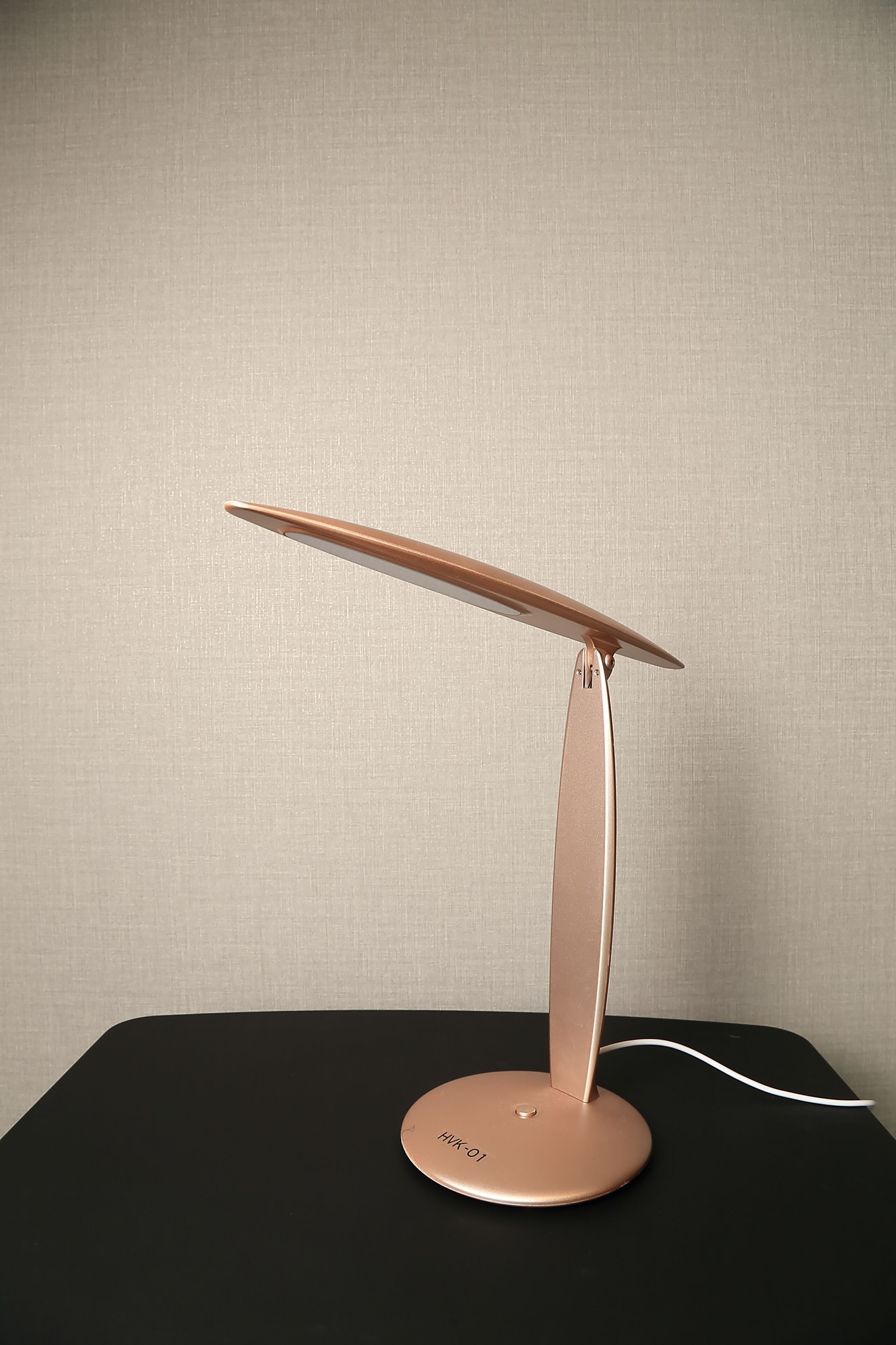 A modern, minimalist table lamp with a sleek design, featuring a circular base and a slender, elongated arm.
