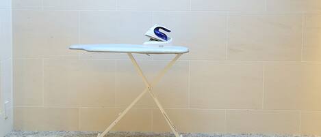 A white ironing board with a blue and white iron on top, placed against a tiled wall.