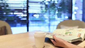 A table with a white cup and a person reading a magazine.