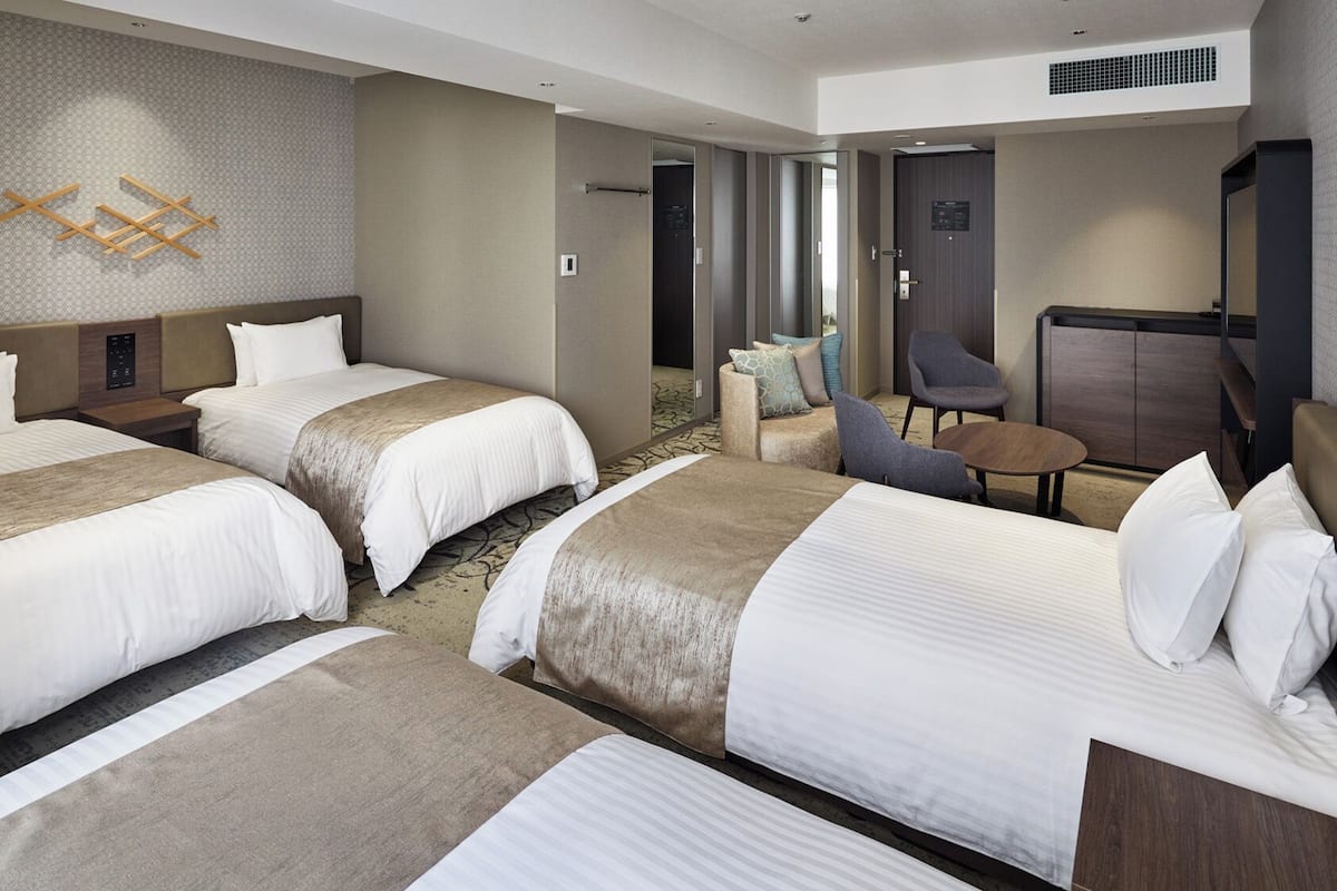 A hotel room with three beds, a seating area with a table, and a TV.