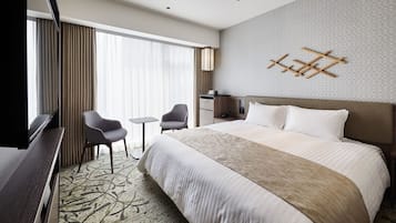 Una habitación de hotel con una cama grande, dos sillones, una mesita, un escritorio y un televisor.