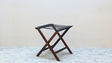 Un taburete pequeño y oscuro de madera con estructura metálica y superficie plana, sobre una superficie blanca con textura, frente a una pared lisa.