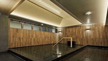 A modern indoor pool area with a wooden wall, a glass enclosure, and a black tiled floor.