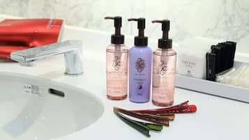 A bathroom with a white sink, three toiletry bottles, a red hairdryer, and a cotton bag.