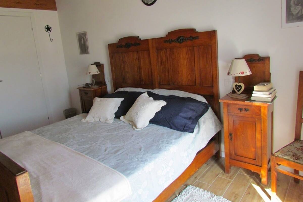 A bedroom with a wooden headboard, a bed with white and blue bedding, a nightstand with a lamp, and a small wooden cabinet.
