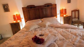 Un letto rifatto con cura, con una coperta a fiori, una testiera in legno e due comodini con candele.