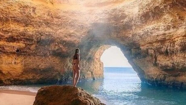 Eine Person steht unter einem natürlichen Felsbogen am Strand.