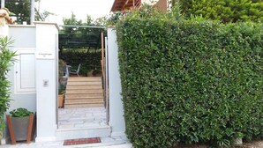 A gated entrance with a wooden staircase leading to a covered area, surrounded by dense green hedges. - Villa near Athens Airport & Rafina (Spata-Artemida)