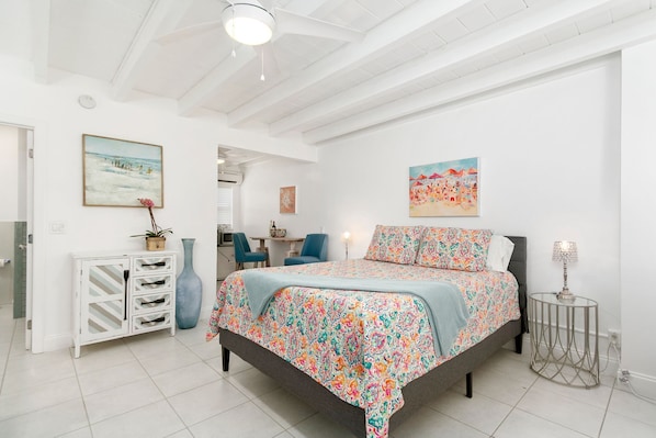 Un dormitorio con cama, mesita de noche, silla, armario y obras de arte en las paredes.