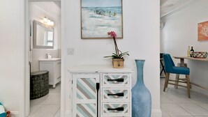 Una cocina moderna con armarios blancos, un jarrón azul y un cuadro de una playa.