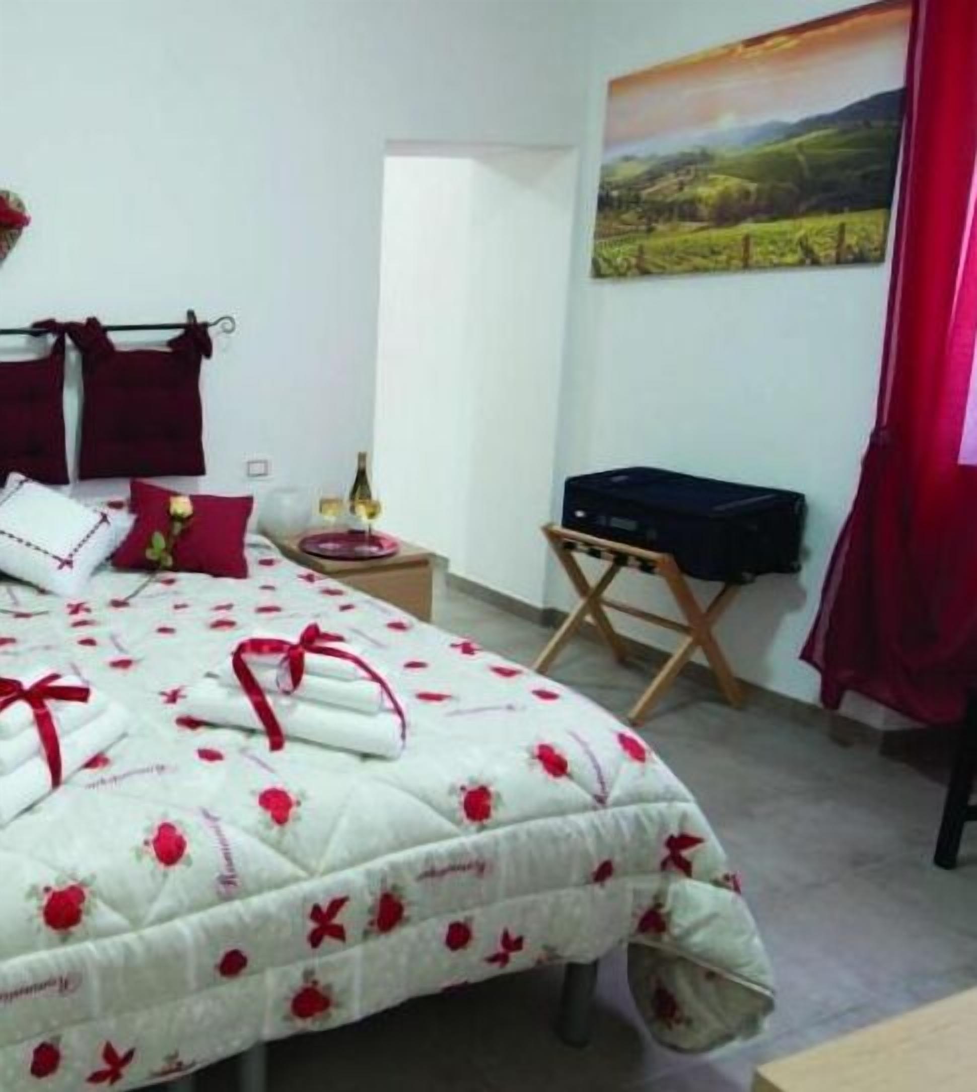 A bedroom with a bed, a nightstand, a suitcase, and a painting on the wall.