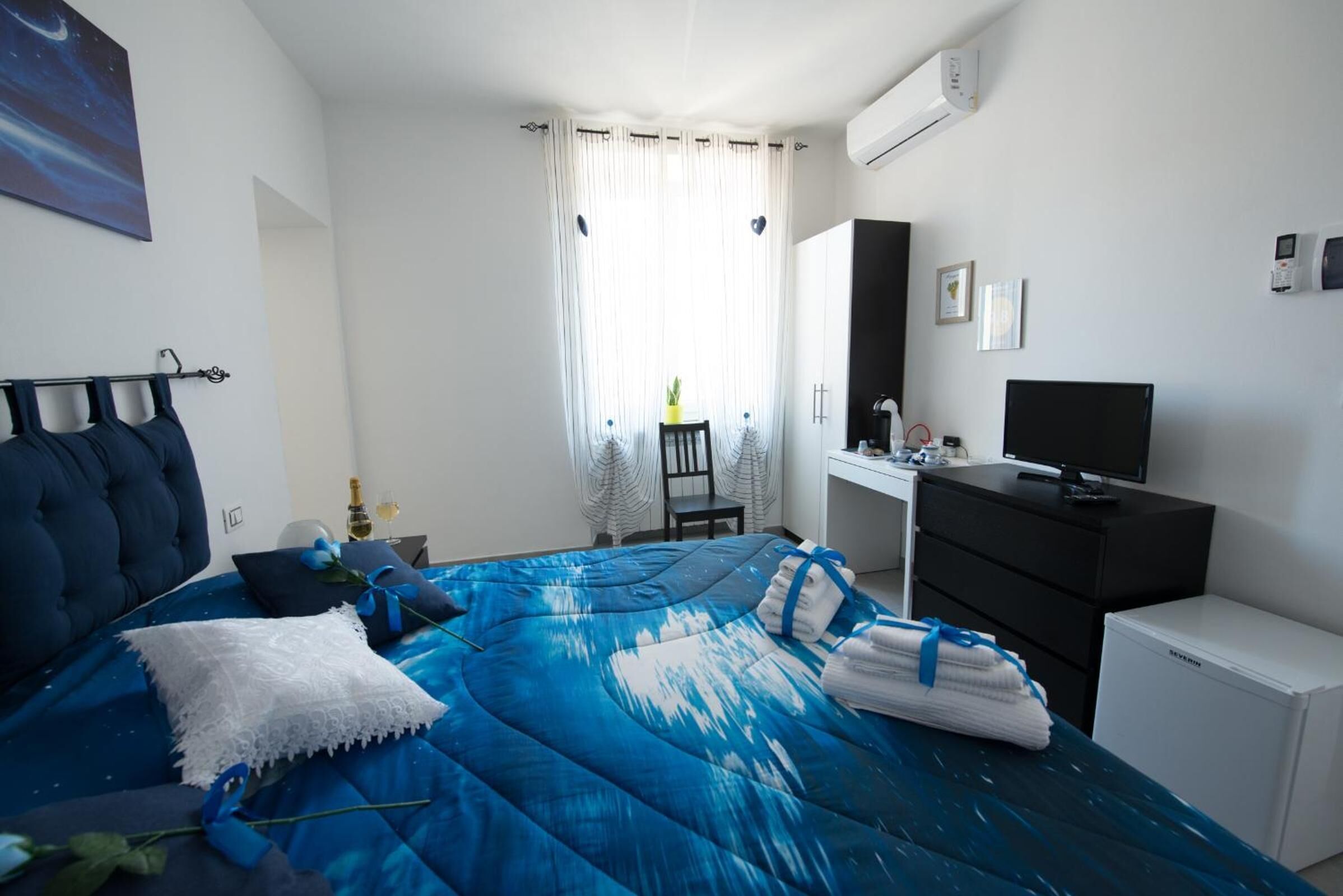 Une chambre avec un lit, un bureau, une chaise, une télévision et un petit réfrigérateur.