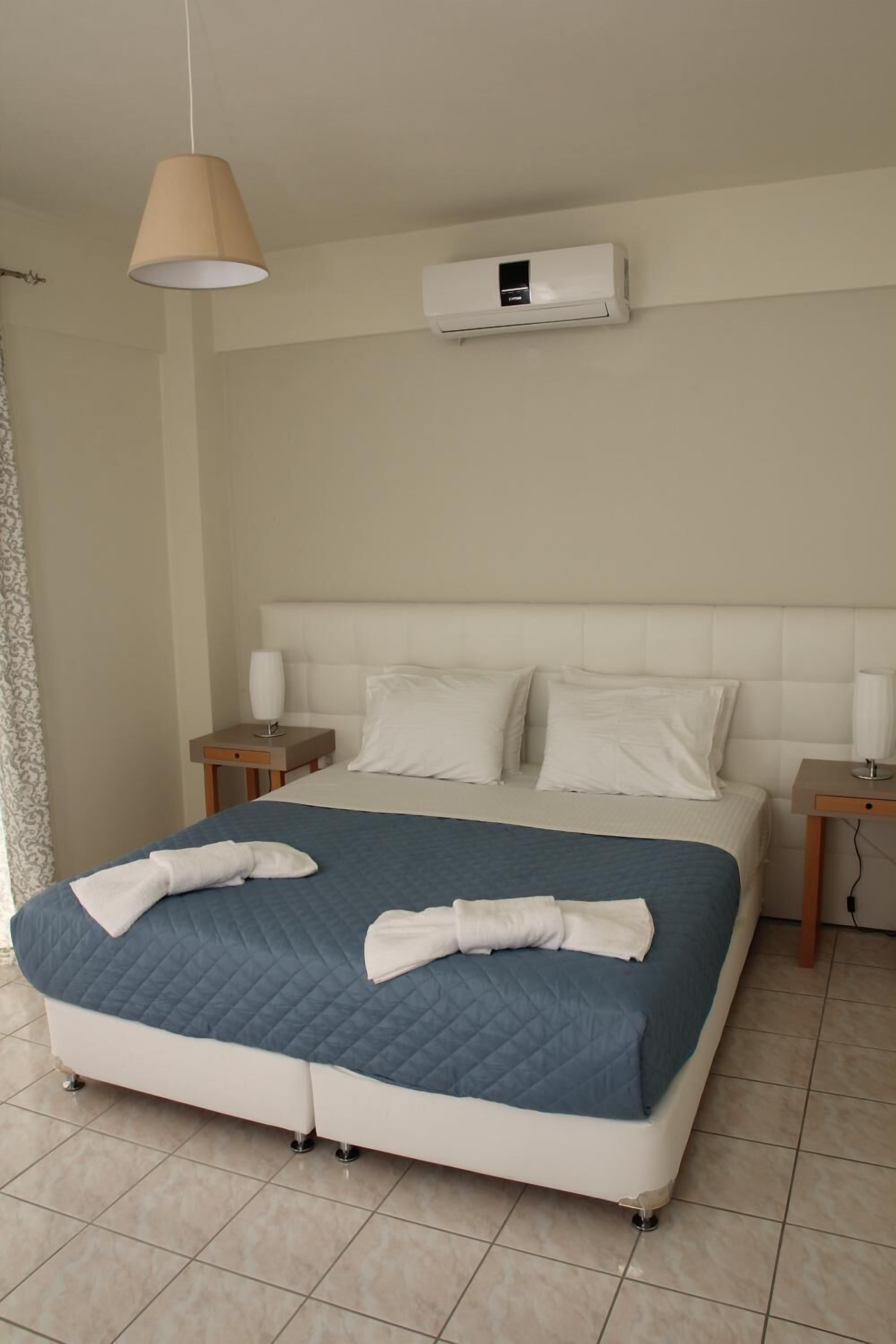 Een hotelkamer met een bed, twee nachtkastjes, een wandairconditioner en een hanglamp.