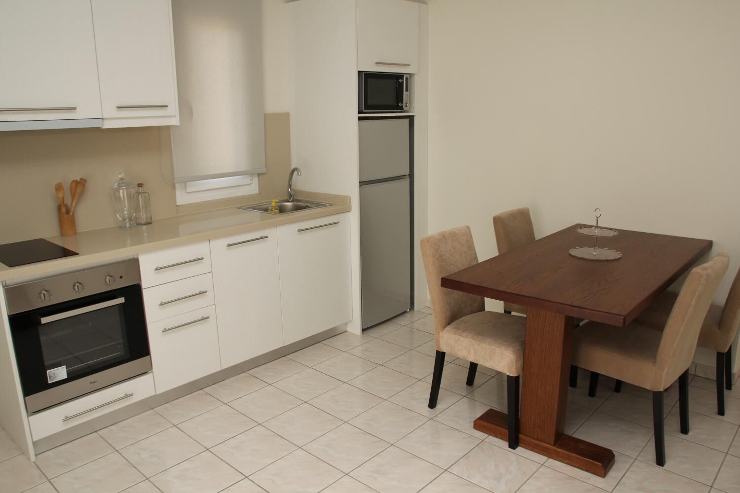 Een moderne keuken met witte kastjes, een inbouwoven, een magnetron en een eettafel met stoelen.