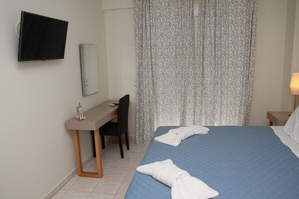 A hotel room with a bed, a desk, a chair, a TV, and a window with curtains. - Holiday Luxury Villas (Faistos)