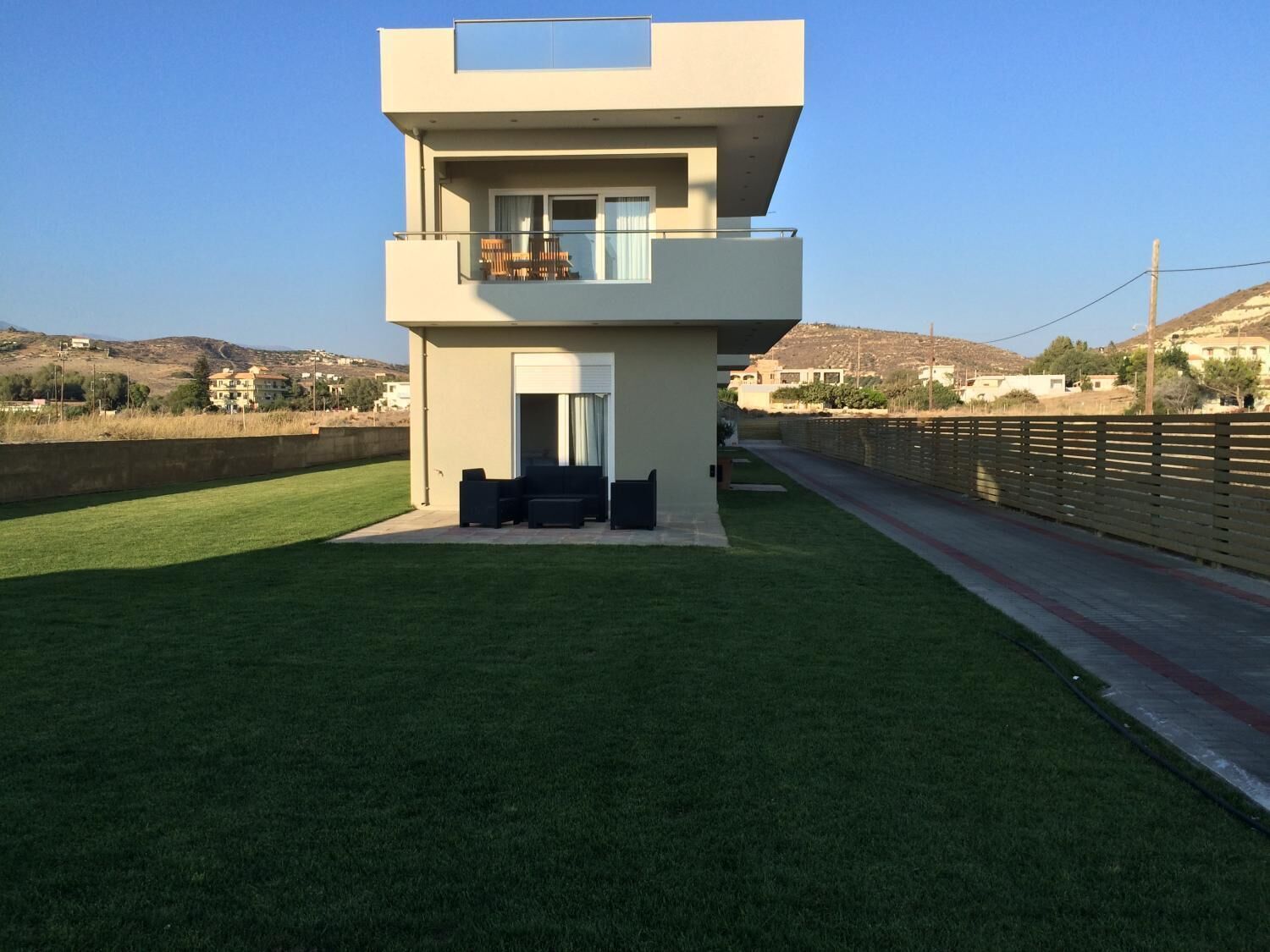 Una casa moderna de dos pisos con techo plano, un balcón con mobiliario exterior y un césped bien cuidado.