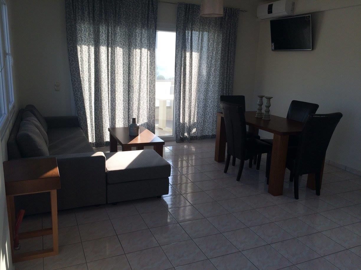 A living room with a sofa, ottoman, dining table, chairs, and a TV mounted on the wall.