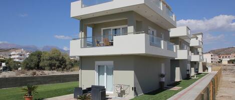 A modern multi-story residential building with a flat roof, large windows, and a balcony.