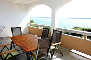 A terrace with a wooden table and chairs, overlooking a body of water. - Apartments Mak (Kolan)
