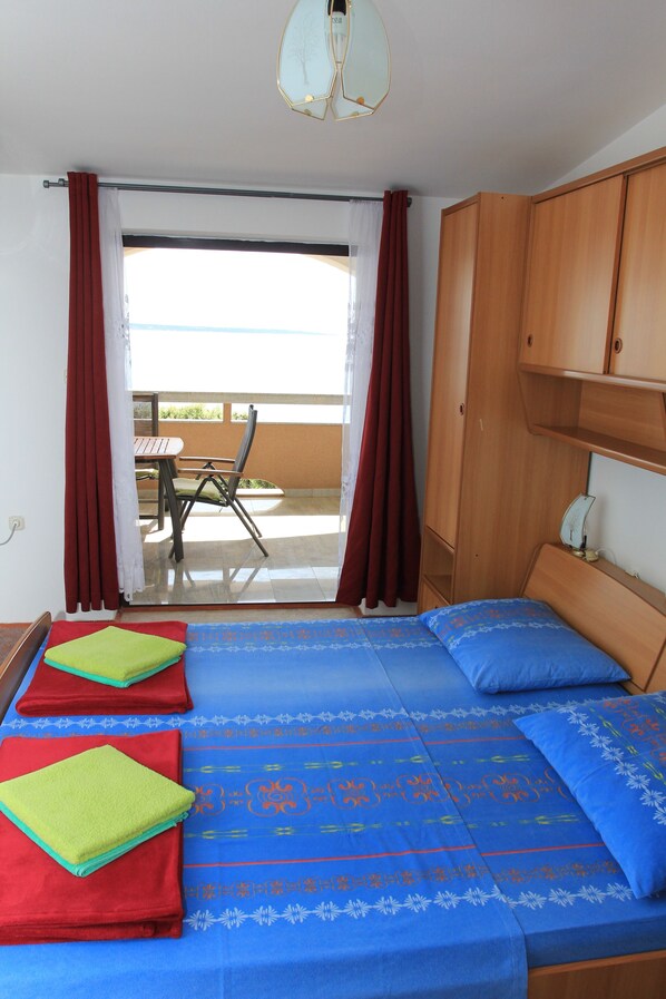 A bedroom with a bed, wooden wardrobe, and a balcony with a table and chair. - Apartments Mak (Kolan)