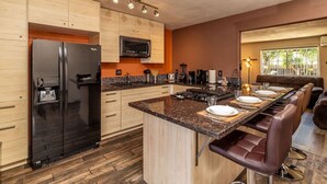 A modern kitchen with a black refrigerator, wooden cabinets, a built-in microwave, and a dining area with a long table and leather chairs. - Giraffe House Chula Vista (Chula Vista)