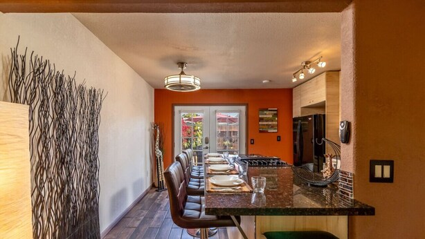 A modern kitchen with a dining area, featuring a long table with chairs, a refrigerator, and a hanging light fixture. - Giraffe House Chula Vista (Chula Vista)