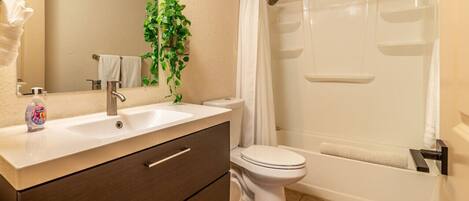 Une salle de bain équipée d’un lavabo, d’un miroir, de toilettes, d’une douche et d’une plante.