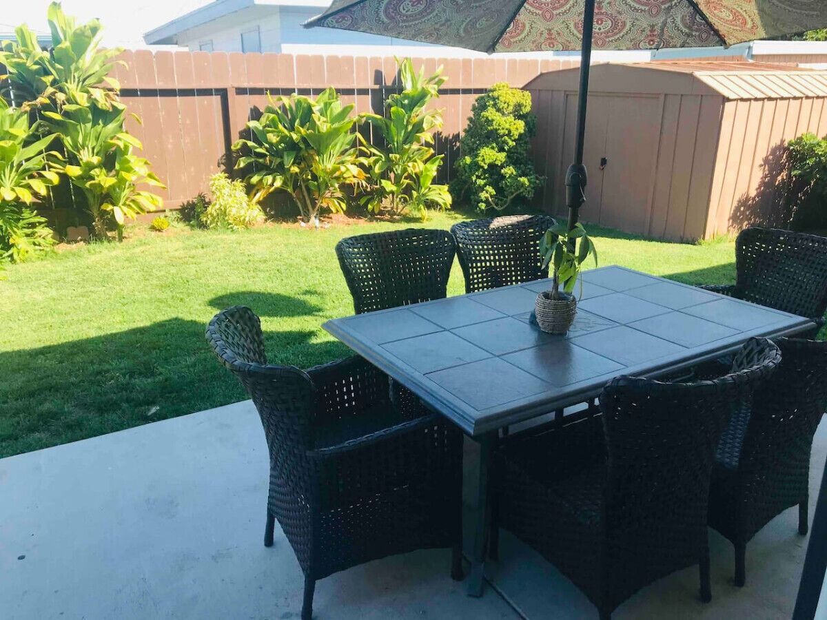 An outdoor patio with a table and chairs, surrounded by a garden and a wooden fence.