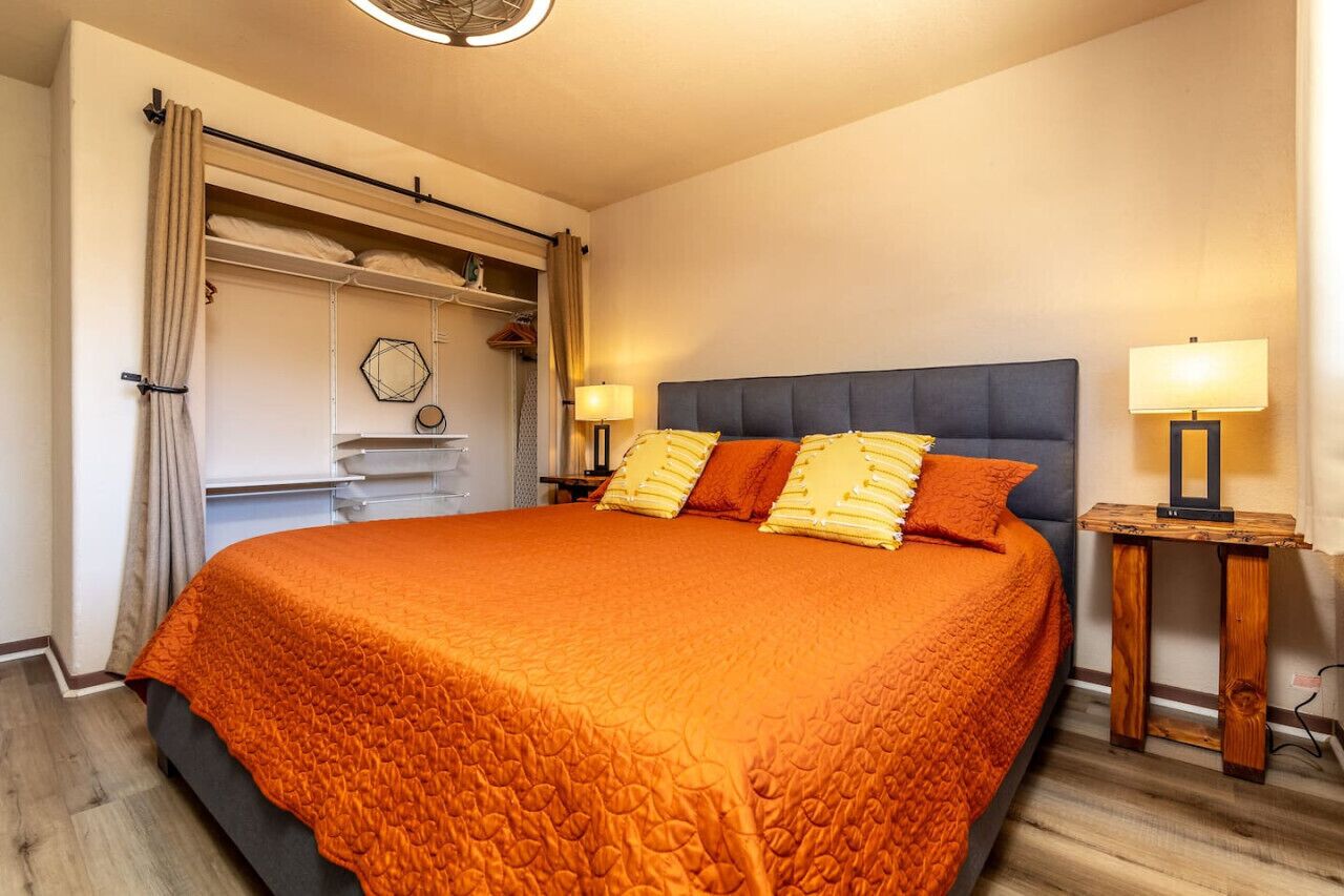 A bedroom with a large bed, two bedside lamps, a wooden nightstand, and a wardrobe with a curtain.