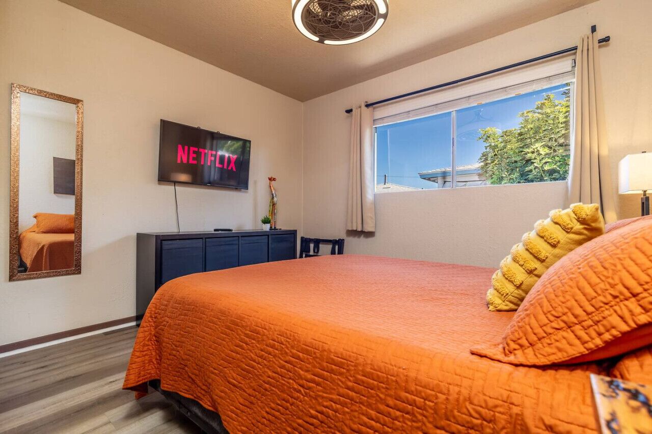 Une chambre d’hôtel avec un lit, un téléviseur affichant le logo « NETFLIX », une fenêtre donnant sur un paysage agréable et un miroir au mur.