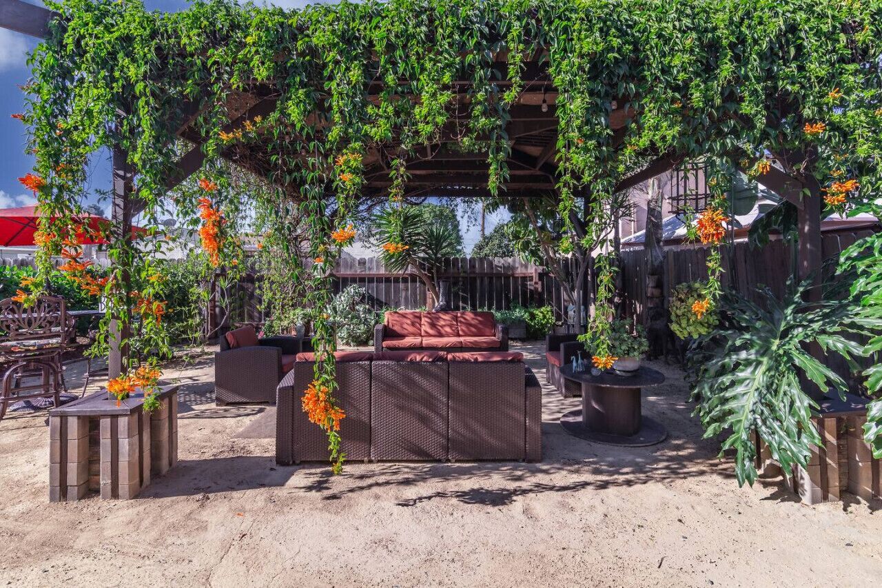 Un espacio de estar al aire libre con pérgola, mobiliario de mimbre y plantas en macetas.