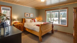 A bedroom with a wooden bed, a nightstand, a lamp, and a window with a view of trees.