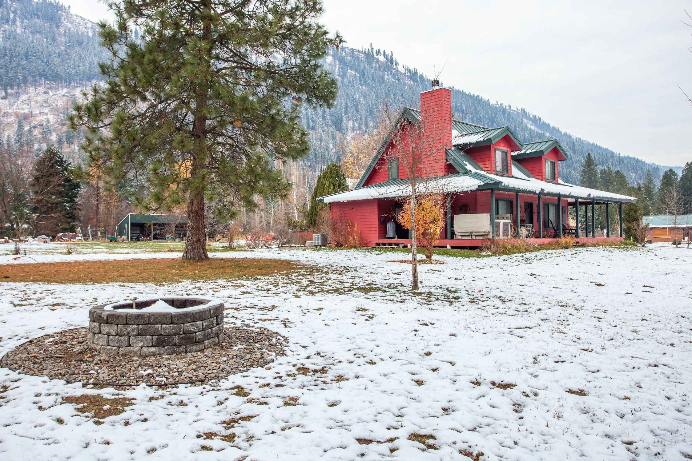 Une maison rouge avec une cheminée, entourée d’un paysage enneigé et avec une montagne en arrière-plan.